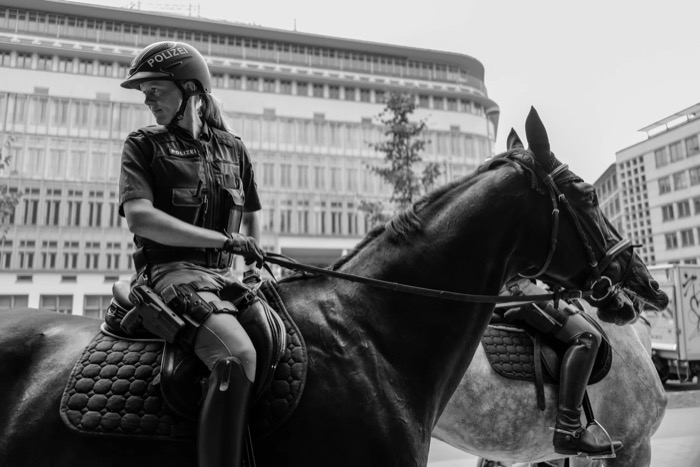 Mounted police officer in a Polizei helmet reins in her horse in front of a curved office facade