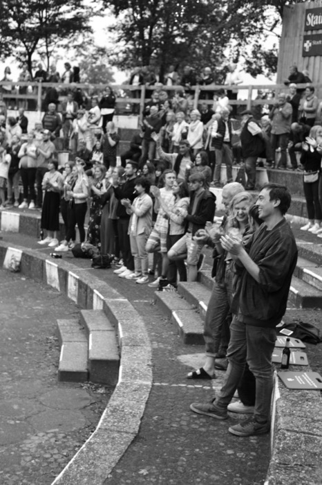 Audience standing and applauding on the curved stone steps of an outdoor amphitheatre