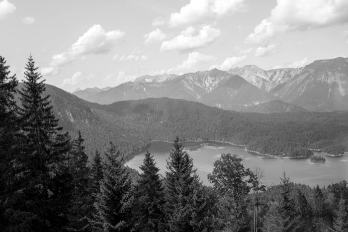 Forested slopes framing a lake below a long mountain ridge and cumulus clouds