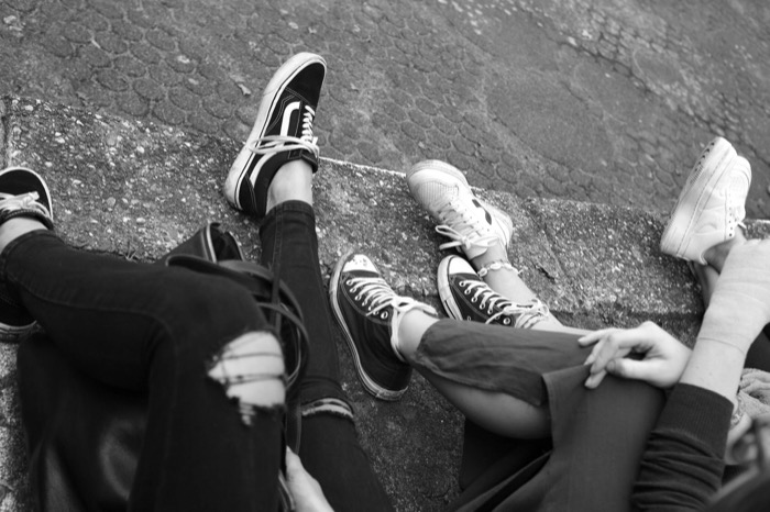 Looking down at four friends' sneakered legs stretched out on a concrete kerb