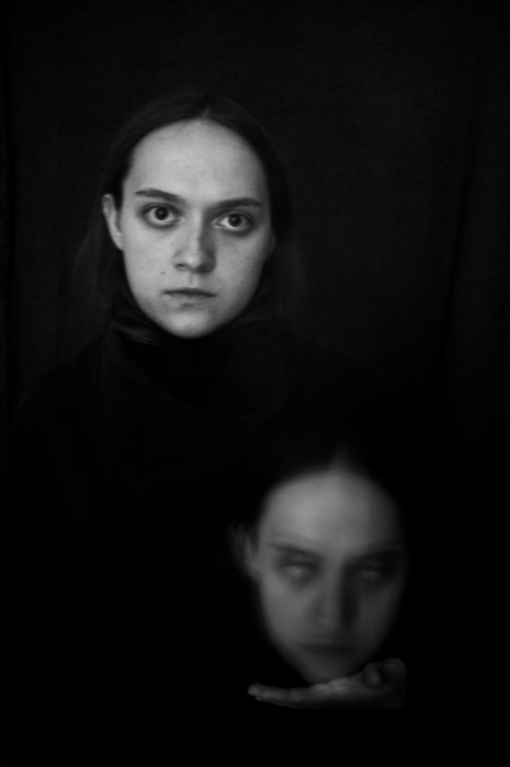 Young woman staring into the camera against black, a second blurred face floating below her