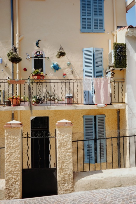 Balcony of a pale house crowded with plants, ornaments and laundry beside blue shutters