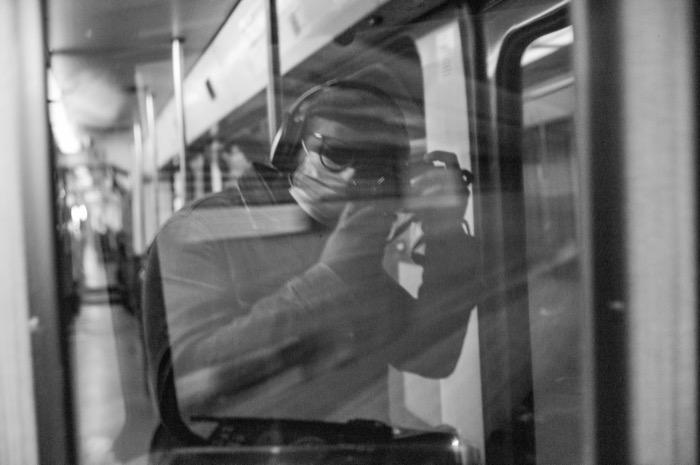 Masked man raising a camera, reflected in the window of a moving train carriage