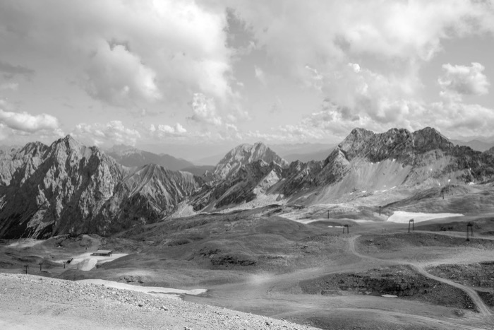 High mountain plateau with ski lift pylons and lingering snow patches, ranges receding under piled clouds