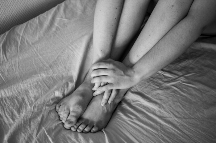 Bare legs drawn up on a creased white bedsheet, hands resting over crossed feet