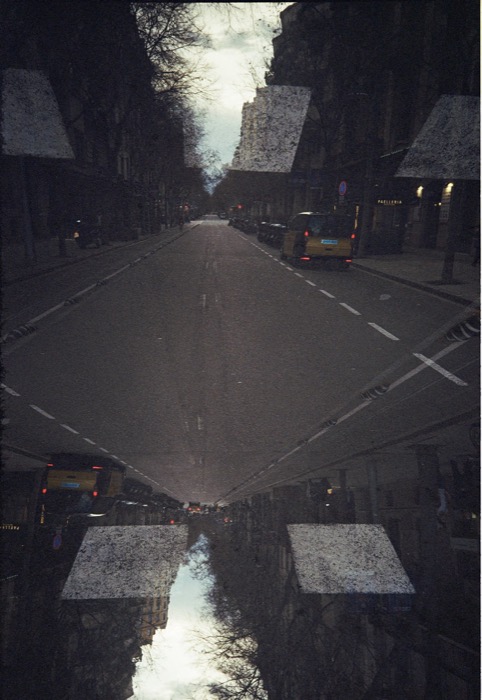 Double-exposed city street mirrored top to bottom, road and awnings meeting at the horizon line