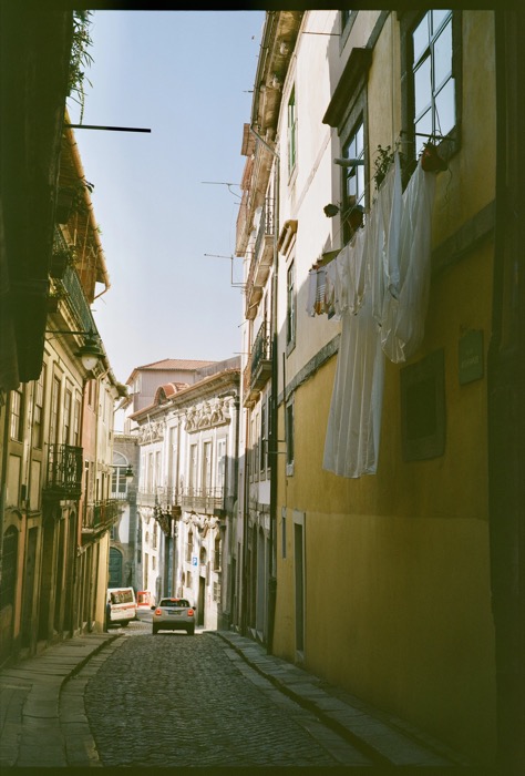 Narrow cobbled hill street with laundry hung from a yellow facade and a car parked below balconies