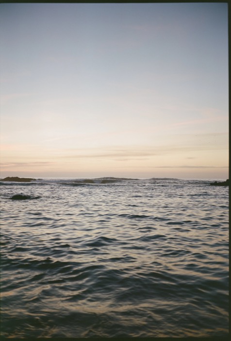 Open sea at dusk, small waves breaking on a low reef under a pale pink and blue sky