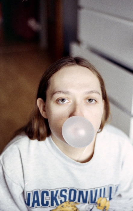 Young woman in a Jacksonville sweatshirt blowing a large bubblegum bubble, staring straight ahead