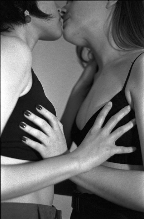 Two women in black tops kissing, hands pressed against each other's chests, cropped close from chin to waist