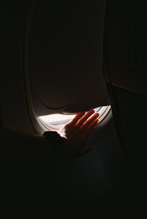 Hand reaching into the sliver of light at a half-closed aeroplane window in a dark cabin