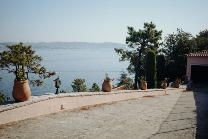 Terracotta urns along a curving villa terrace above a hazy blue bay and distant coastline