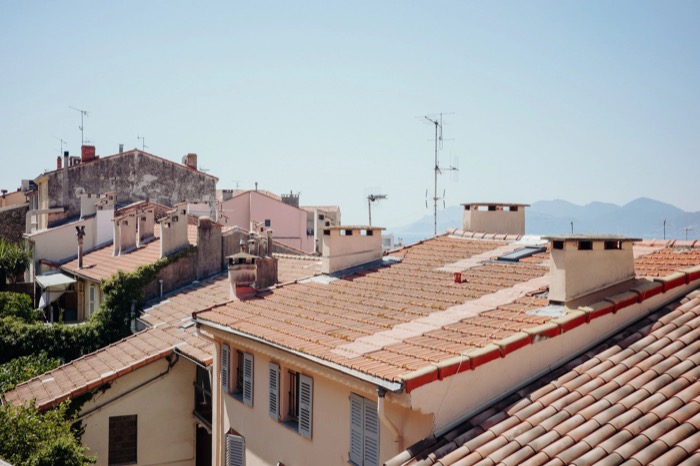 Terracotta rooftops, chimneys and aerials of a Mediterranean old town with hills across the bay
