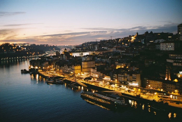 Riverside old town stacked up a hillside at dusk, quayside lights reflected in the water