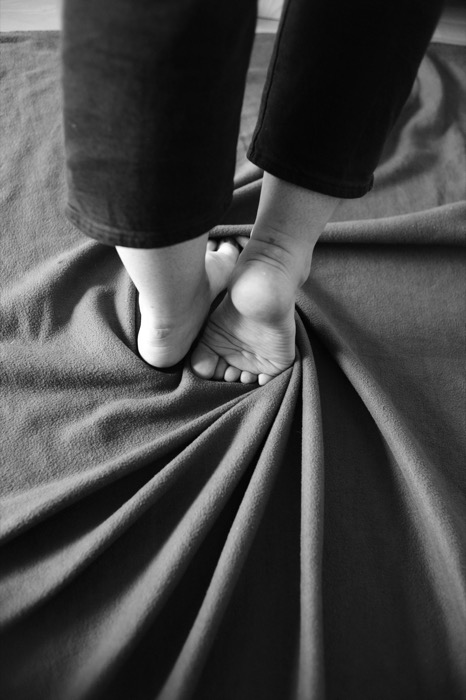 Bare feet standing on a blanket whose folds radiate outward across the floor