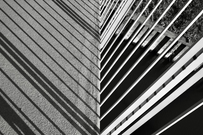 Diagonal railing bars and their striped shadows converging on a concrete wall's edge