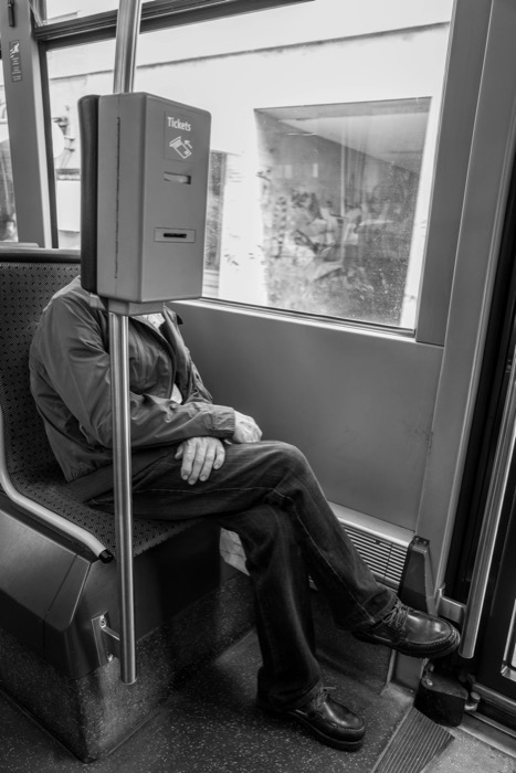 Seated tram passenger whose head is hidden behind a ticket validator marked Tickets