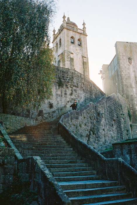 Wide stone stairway climbing toward a cathedral bell tower, a lone figure pausing at the top