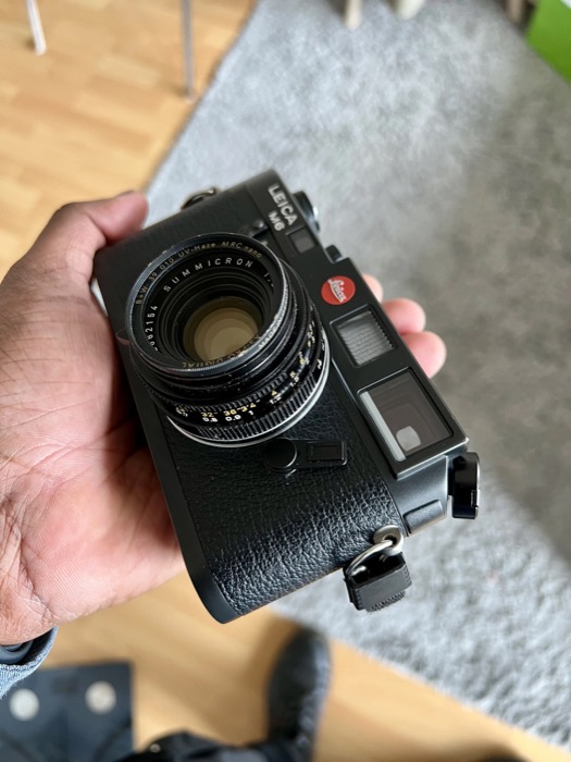 Hand holding a black rangefinder camera with a Summicron lens over a grey carpet