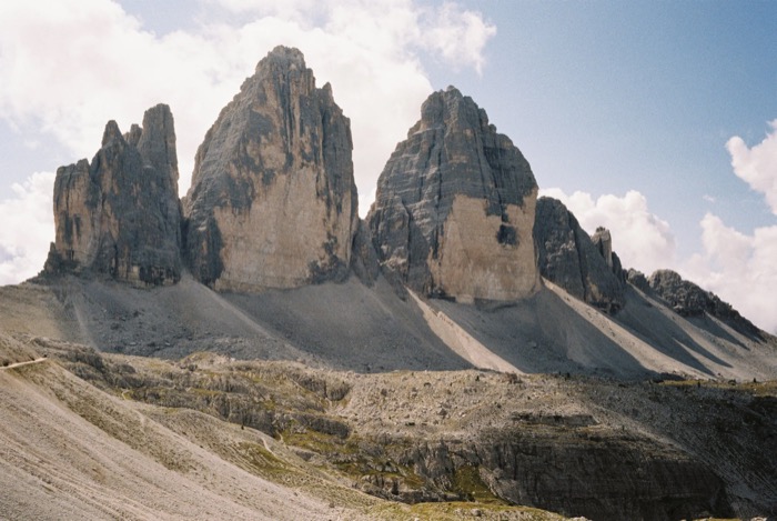 Three jagged limestone peaks rising over grey scree slopes under scattered cloud