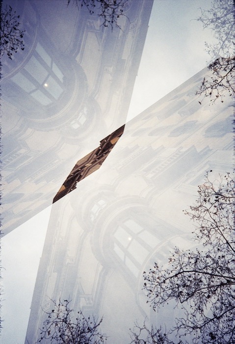 Double exposure of a church tower crossing itself diagonally against sky and bare branches