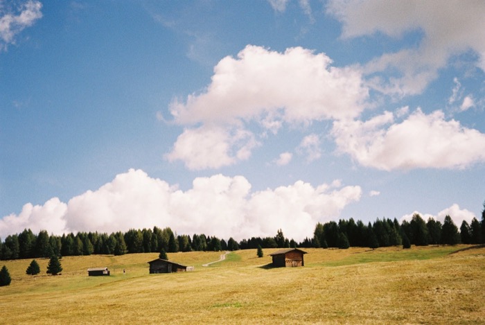 Two small wooden barns on a wide meadow under towering cumulus clouds