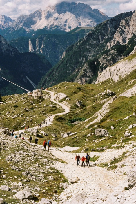Line of hikers descending a winding gravel path into a deep mountain valley