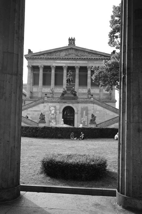 Alte Nationalgalerie seen between two massive columns, people sitting on the lawn in front