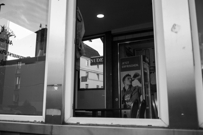Empty snack bar seen through its window, a denim jacket hung by the door and a drinks fridge inside