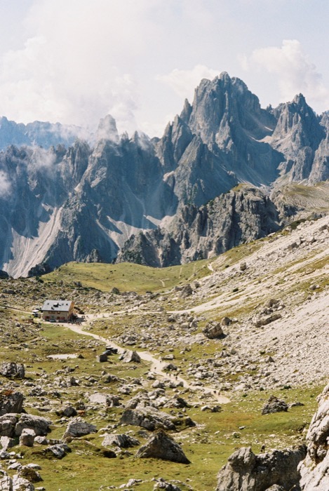 Small alpine hut at the end of a gravel track in a rocky basin beneath toothed grey peaks